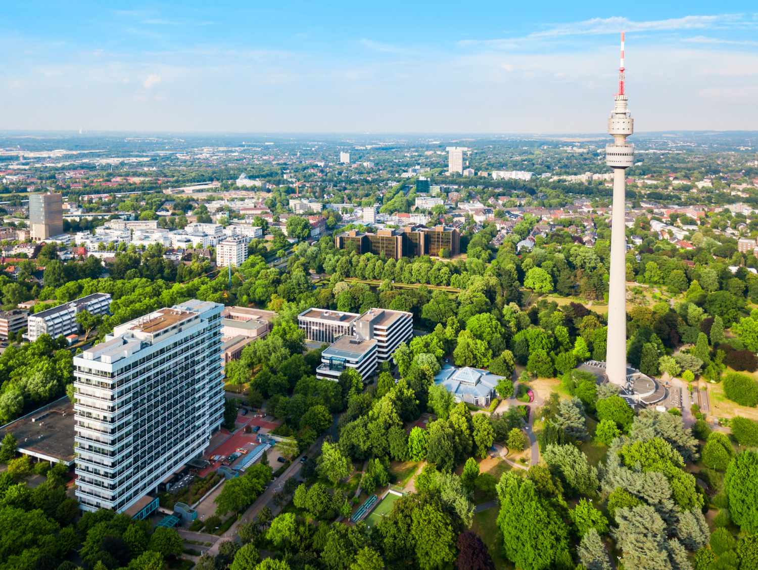 Aerial view of a cityscape with a prominent television tower surrounded by greenery.