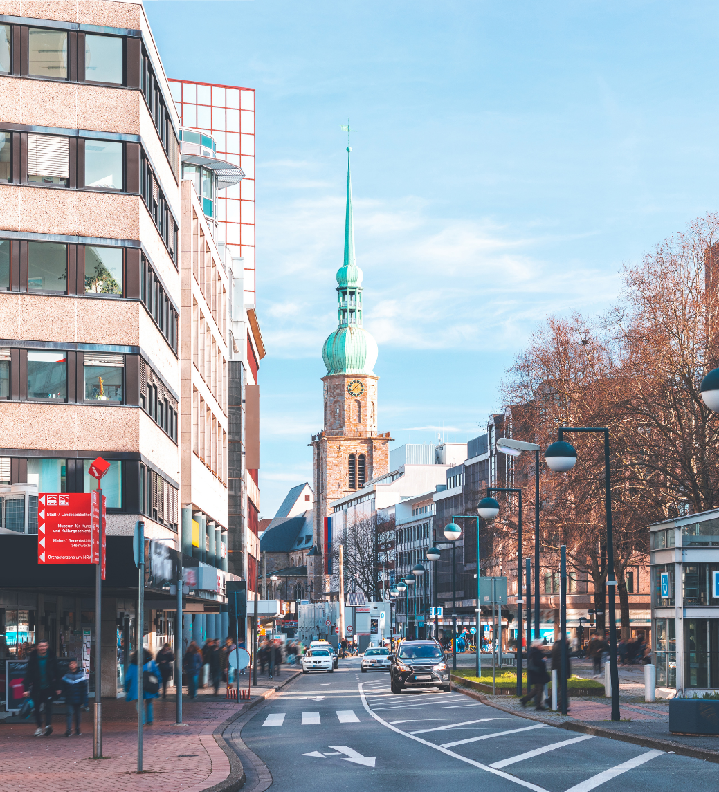 City street with modern buildings and a church steeple under a clear blue sky.
