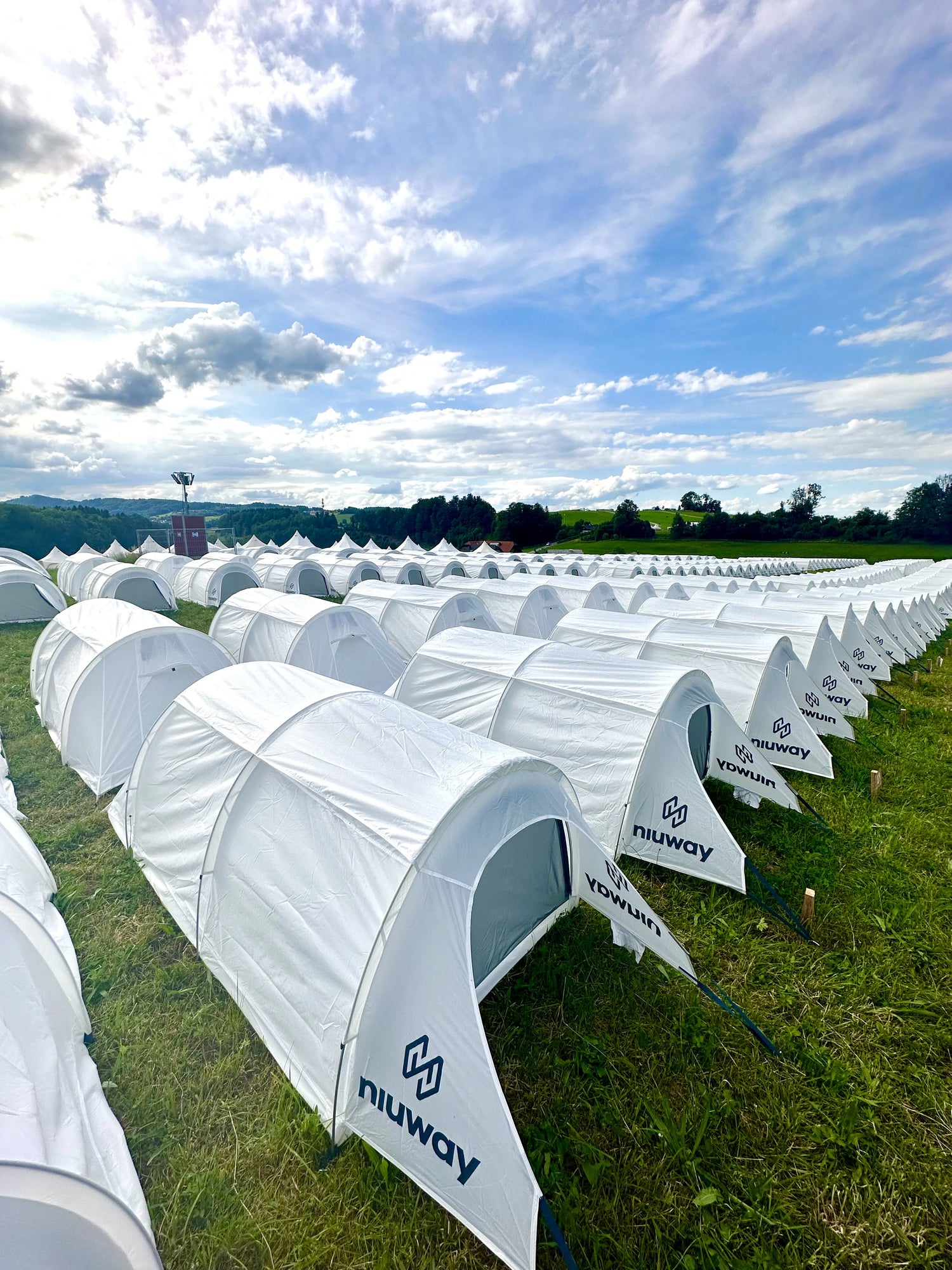 Multiple white tents with 'niuway' branding set up in a field under a blue sky with clouds.